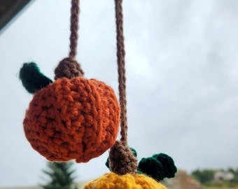 May include: Two crocheted pumpkins hanging from a brown string. The top pumpkin is orange and the bottom pumpkin is yellow.