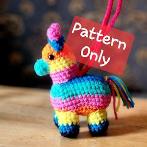 May include: A colorful, crocheted donkey piñata with a rainbow design. The piñata has a pink mane, blue and orange accents, and a multi-colored tail. The text "Pattern Only" is displayed on a red rectangle.