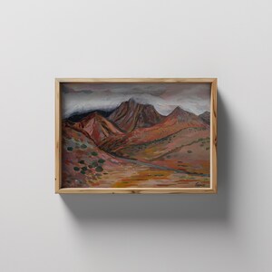 May include: A framed painting of a mountain range with a cloudy sky. The mountains are painted in shades of brown, red, and purple. The sky is a light blue with white clouds.