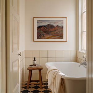 May include: A white bathtub with a white towel draped over the side, sitting in a bathroom with white tile walls and a framed painting of a mountain landscape above the tub.