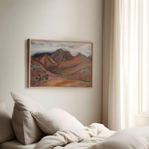 May include: A framed painting of a mountain range with a cloudy sky. The mountains are painted in shades of brown, red, and orange. The sky is a light blue with white clouds.