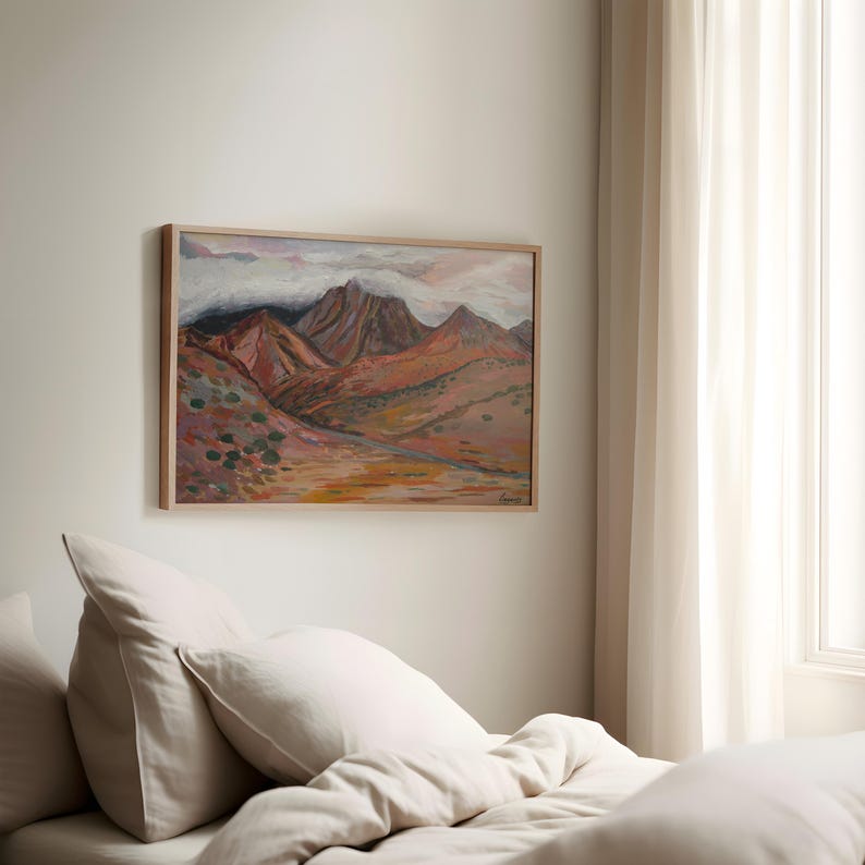 May include: A framed painting of a mountain range with a cloudy sky. The mountains are painted in shades of brown, red, and orange. The sky is a light blue with white clouds.