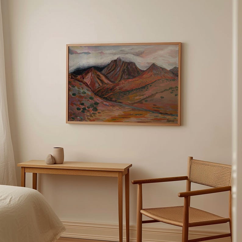 May include: A framed painting of a mountain range with a cloudy sky. The mountains are painted in shades of red, orange, and brown. The sky is painted in shades of blue and white.