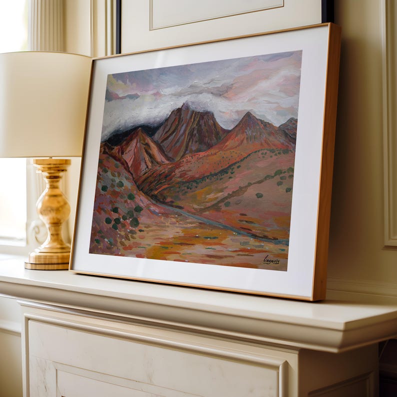 May include: A framed painting of a mountain range with a cloudy sky. The mountains are painted in shades of brown, red, and purple. The sky is painted in shades of blue, pink, and white.