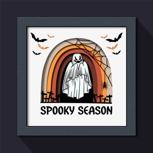 May include: A white ghost with a spooky face stands in front of a layered rainbow arch with a spider web and bats. The text "Spooky Season" is written below the arch.