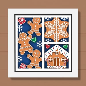 May include: A white frame with a blue background featuring gingerbread people, a gingerbread house, and a snowflake. The gingerbread people are decorated with white icing and red candy. The gingerbread house has white icing and red candy canes. The snowflake is white.