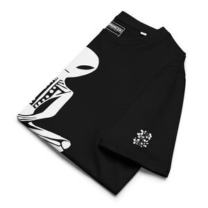 Puede incluir: Camiseta negra con un gr&aacute;fico blanco de un esqueleto alien&iacute;gena con el texto "MANCLA" en la etiqueta.