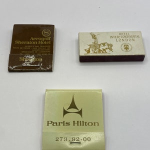 May include: Three matchbook covers. The first is brown with gold lettering and the text "Aerogolf Sheraton Hotel". The second is white with gold lettering and the text "Hotel InterContinental London". The third is white with gold lettering and the text "Paris Hilton 273.92-00".