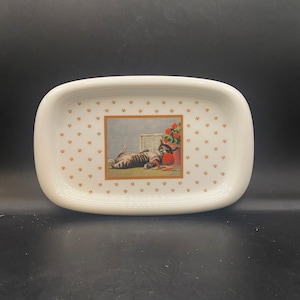 May include: White ceramic rectangular tray with a gold paw print pattern. The center of the tray features a rectangular image of a cat playing with a ball of yarn.