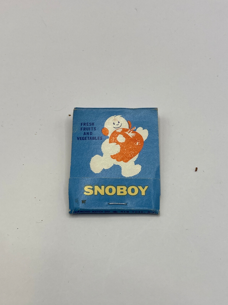 May include: A blue matchbook with a cartoon snowman holding a red apple. The text on the matchbook reads "Fresh Fruits and Vegetables" and "Snoboy". The bottom of the matchbook says "Diamond Match Div. New York, N.Y."