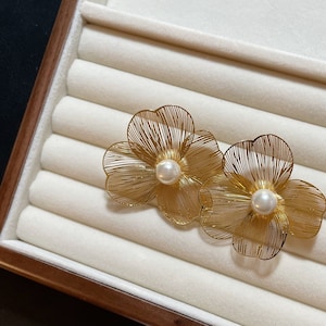 Pode incluir: Um par de brincos de ouro em forma de flor com um detalhe de pérola em cada flor.