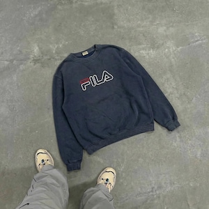 K&ouml;nnte beinhalten: Ein marineblaues Fila-Sweatshirt mit dem Markenlogo in Wei&szlig;, Rot und Marineblau. Das Sweatshirt hat einen Rundhalsausschnitt und scheint aus einem weichen Material zu bestehen. Das Sweatshirt liegt auf einer grauen Oberfl&auml;che.