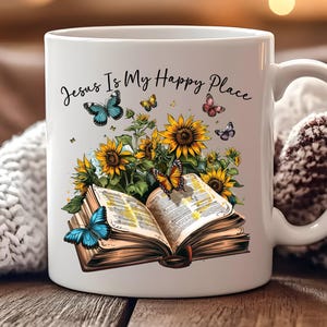 May include: White ceramic mug featuring the text "Jesus Is My Happy Place." The mug is decorated with a colorful illustration of sunflowers, butterflies, and an open book. The design includes blue, yellow, and orange hues.