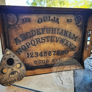 May include: A wooden Ouija board with a planchette, featuring the letters of the alphabet, numbers 1-9 and 0, and the words "YES", "NO", "GOOD BYE", and "HELLO".