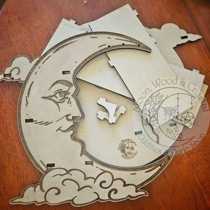 Puede incluir: Un kit de manualidades de madera para ensamblar una estantería de luna y nube. La luna tiene una cara y la nube tiene un diseño de remolino. El kit incluye varias piezas de madera.