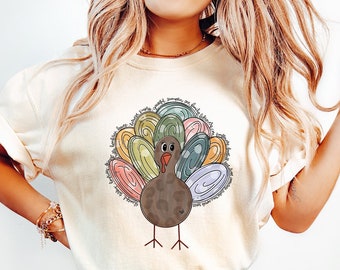 May include: A white t-shirt with a colorful turkey graphic. The turkey has a brown body and a colorful tail made of swirls and dots. The text "IVORY" is visible in the lower right corner of the image.