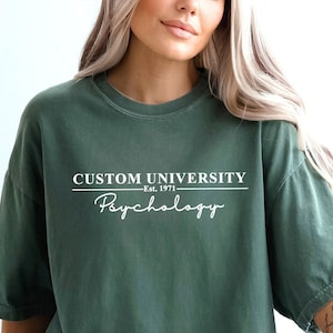 May include: A moss green oversized t-shirt with the text "CUSTOM UNIVERSITY Est. 1971 Psychology" printed in white.