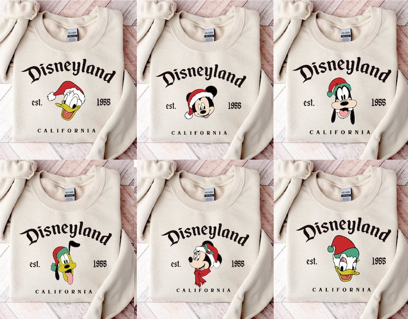 May include: Six different designs of beige sweatshirts with the text "Disneyland est. 1955 California" and a cartoon character wearing a Santa hat. The characters are Mickey Mouse, Donald Duck, and Goofy.