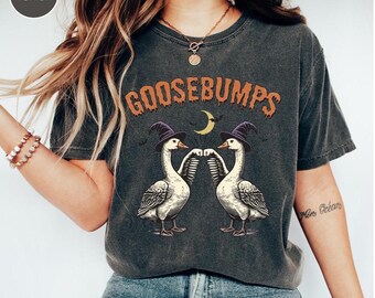 May include: Dark gray t-shirt with the word "GOOSEBUMPS" in orange lettering. The shirt features a graphic of two geese wearing witch hats, with a crescent moon and bats. The shirt is a vintage style.