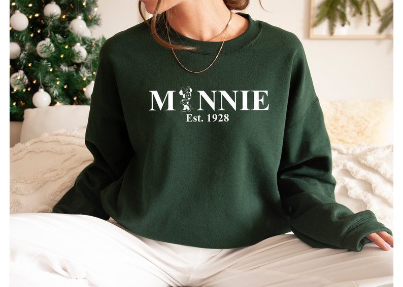 Pu&ograve; includere: Una felpa verde scuro con una grafica bianca di Minnie Mouse e il testo "Minnie Est. 1928".