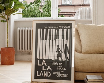 May include: A black and white poster with a piano keyboard design and silhouettes of two people walking. The text reads "La La Land" with the names Ryan Gosling and Emma Stone. The poster is framed in a wooden frame.