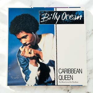 May include: Album cover for Billy Ocean's "Caribbean Queen." The cover features a portrait of Billy Ocean against a blue background. The album title and artist's name are displayed in white and black text.