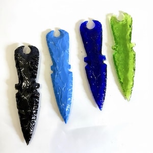 Puede incluir: Cuatro dagas decorativas de vidrio en negro, azul, azul oscuro y verde. Cada daga tiene una superficie texturizada y un agujero en la parte superior. Las dagas están dispuestas sobre un fondo blanco.