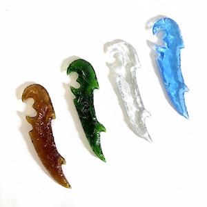 May include: Four decorative glass daggers in shades of amber, green, clear, and blue. Each dagger has a curved blade and a stylized handle. The daggers are arranged diagonally against a white background.