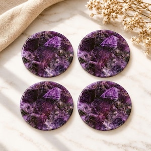 May include: A set of four circular coasters crafted from polished amethyst stone, featuring deep purple and violet hues with natural crystalline patterns and jagged, dark inclusions visible throughout the smooth, reflective surface of each piece.