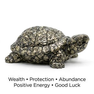May include: A detailed, metallic-looking turtle figurine. The sculpture has a textured surface with a mix of silver and gold tones. The text below the turtle reads: Wealth, Protection, Abundance, Positive Energy, and Good Luck.
