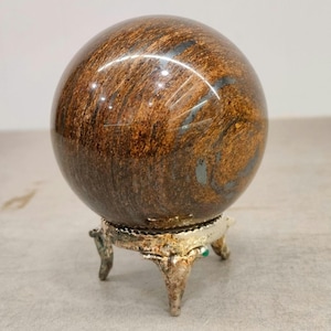 May include: A brown and black orb with a swirling pattern, displayed on a silver-colored, three-legged stand. The orb has a polished, reflective surface. The stand has a decorative, ornate design.