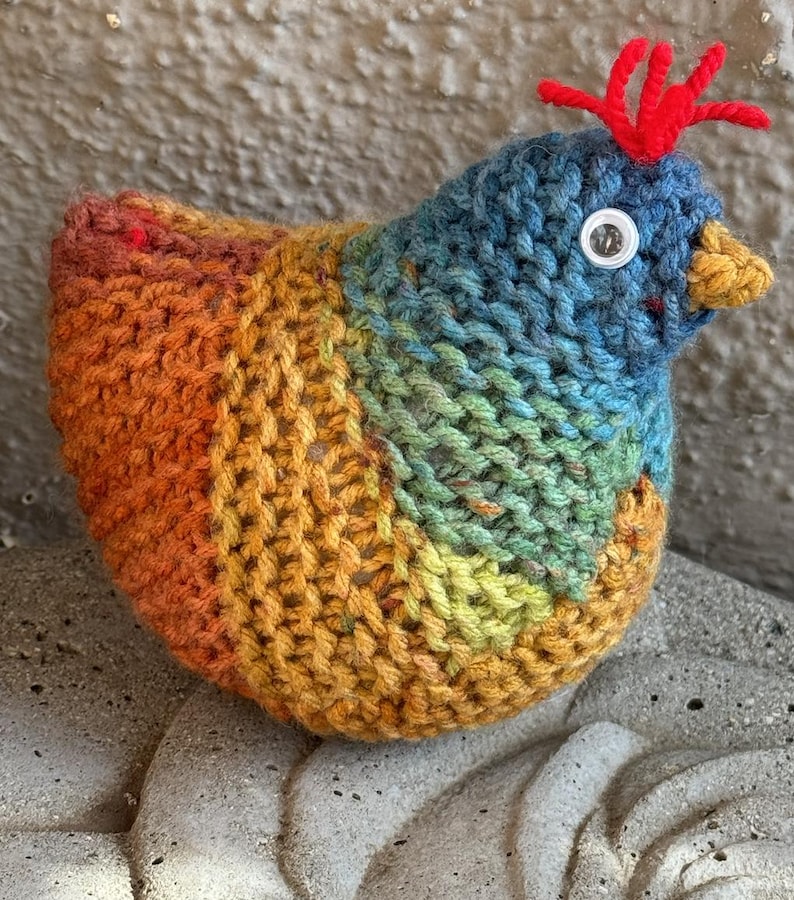 K&ouml;nnte beinhalten: Ein gestricktes Regenbogen-H&uuml;hner-Spielzeug mit rotem Kamm und einem wei&szlig;en Knopf-Auge.