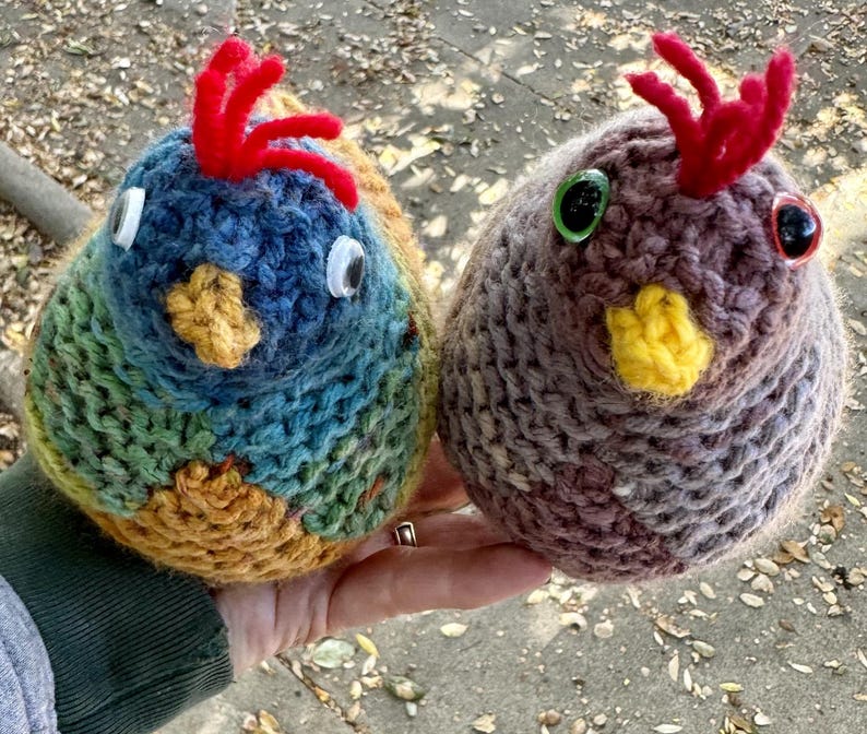 K&ouml;nnte beinhalten: Zwei gestrickte Vogelornamente, eines blau und gr&uuml;n mit roten Akzenten und das andere braun mit gelben Akzenten. Beide haben gro&szlig;e Plastikaugen.