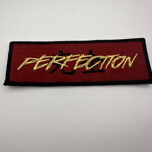 May include: A red embroidered patch with black stitching and gold lettering that reads "PERFECTION".