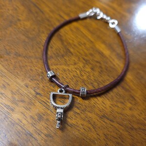 Op de afbeelding: Een bruin leren armband met een zilveren sleutelbedel en decoratieve zilveren kralen.