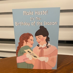 May include: A greeting card with a blue background featuring two women in period dress. The card reads "Make Haste! It's the Birthday of the Season."
