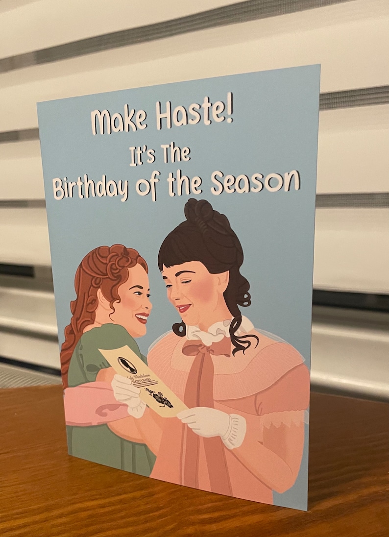 May include: A blue card with the text "Make Haste! It's the Birthday of the Season" and an illustration of two women in period clothing smiling at each other.