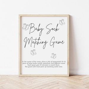 May include: A printable sign for a baby shower game called "Baby Sock Matching Game". The sign has a black and white design with illustrations of baby socks. The text on the sign instructs guests to match pairs of baby socks in a timed game.