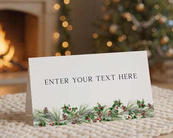 May include: A white folded card featuring the black text ENTER YOUR TEXT HERE centered on the front. The bottom edge of the card is decorated with a horizontal illustration of green pine needles, holly leaves, and small red berries.