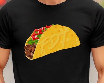 May include: Black t-shirt featuring a colorful illustration of a taco. The taco is filled with meat, lettuce, and tomatoes, with the letters "FOT" on the tortilla. The shirt is a crew neck style.