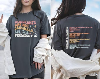 May include: Dark gray t-shirt with the text "IMMIGRANTS ARE NOT CRIMINALS BUT THE PRESIDENT IS" in a retro font. The back of the shirt lists "CHARGES & FELONIES" with details about legal cases.
