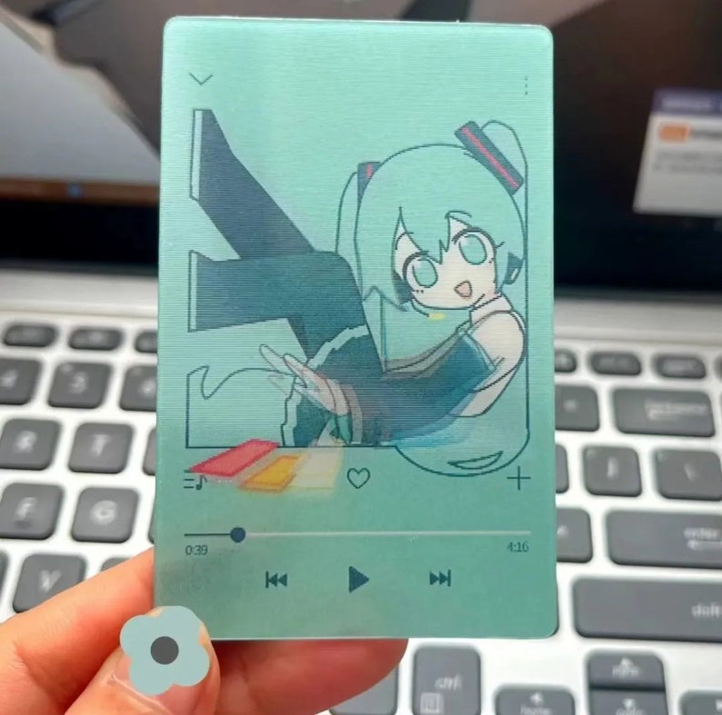 May include: A teal blue card with a cartoon illustration of a female anime character with long green hair. The character is wearing a black and white outfit and is holding a microphone. The card has a music player interface with a play button, rewind button, and fast forward button. The time is 0:29 and 4:16.