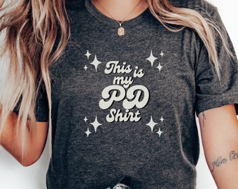 May include: A dark gray t-shirt with the text "This is my PD Shirt" in white with a retro font and sparkling stars around the text.