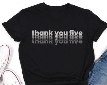 May include: Black t-shirt with the text "thank you five" in a layered, gray font. The shirt is paired with blue jeans and white canvas sneakers with red trim.