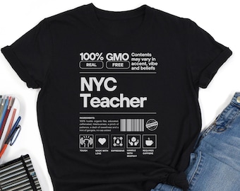 May include: Black t-shirt with white text that reads "100% GMO REAL FREE" and "NYC Teacher". The shirt has a graphic of a product label with the text "INGREDIENTS: 100% hustle, organic flex, educated caffeine, happiness, a pinch of patience, a dash of sweetness and a hint of gangsta, no cap added." The label also has icons for "TOUGH", "MADE WITH LOVE", "EXPRESSIVE", "HANDLE WITH RESPECT", and "REQUIRES CAFFEINE".