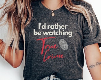May include: A dark grey t-shirt with the text "I'd rather be watching True Crime" in white and red lettering. A fingerprint graphic is next to the text.