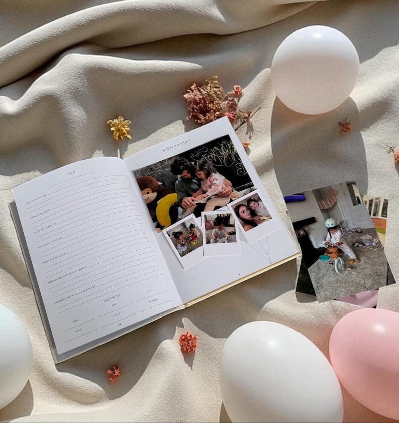 Puede incluir: Un diario abierto con p&aacute;ginas rayadas y un borde dorado, con fotograf&iacute;as y las palabras "Happy Birthday". El diario est&aacute; rodeado de elementos decorativos, incluyendo adornos blancos y rosas en forma de huevo y flores secas, todo sobre una tela beige.