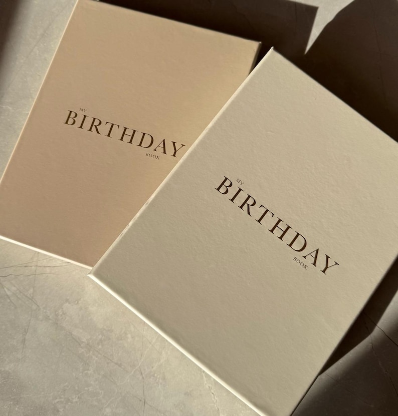 Puede incluir: Dos libros de tapa dura con el texto "MY BIRTHDAY BOOK" en una fuente serif. Un libro es de color beige claro, y el otro es de un beige ligeramente m&aacute;s oscuro. Los libros son rectangulares y parecen diarios o cuadernos.