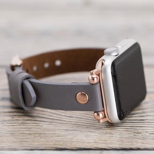 May include: A gray leather watch band with rose gold accents and a silver Apple Watch.