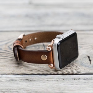 May include: A brown leather watch band with rose gold accents and a silver Apple Watch.